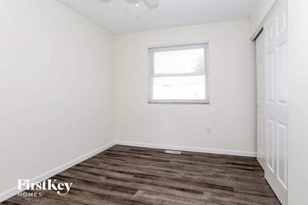 a bedroom with white walls and wood flooring and a window