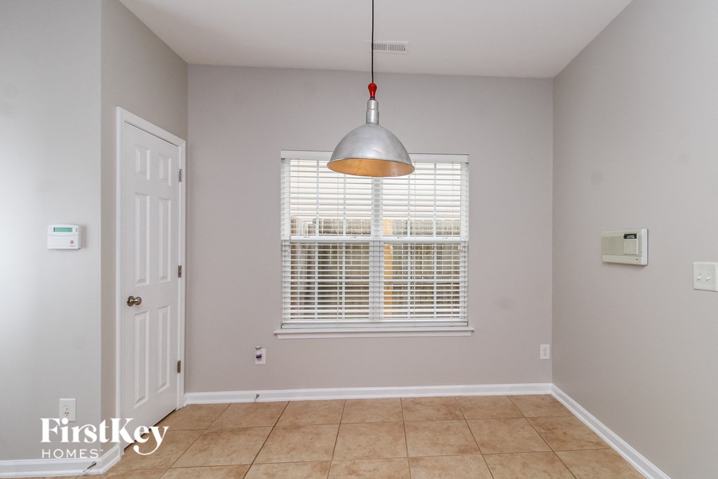 A room with a white door, a window with blinds, and a pendant light hanging from the ceiling.