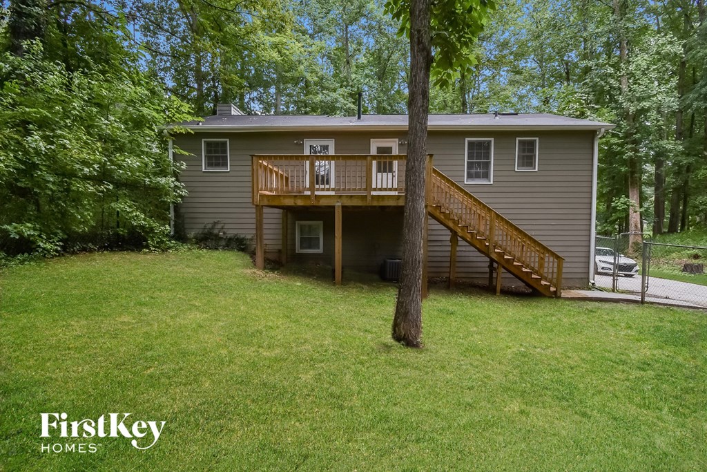 A house with a deck and stairs is surrounded by trees.