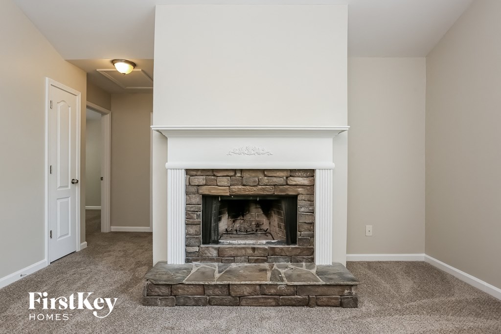 A well-lit room with a stone fireplace and a carpeted floor.