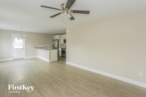 an empty living room with a ceiling fan and a kitchen