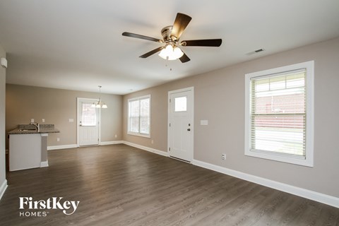 an empty living room with a ceiling fan and a kitchen