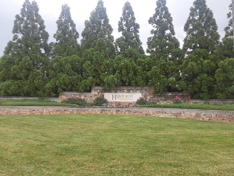 A sign that says "Huntscrest" is in front of a row of trees.