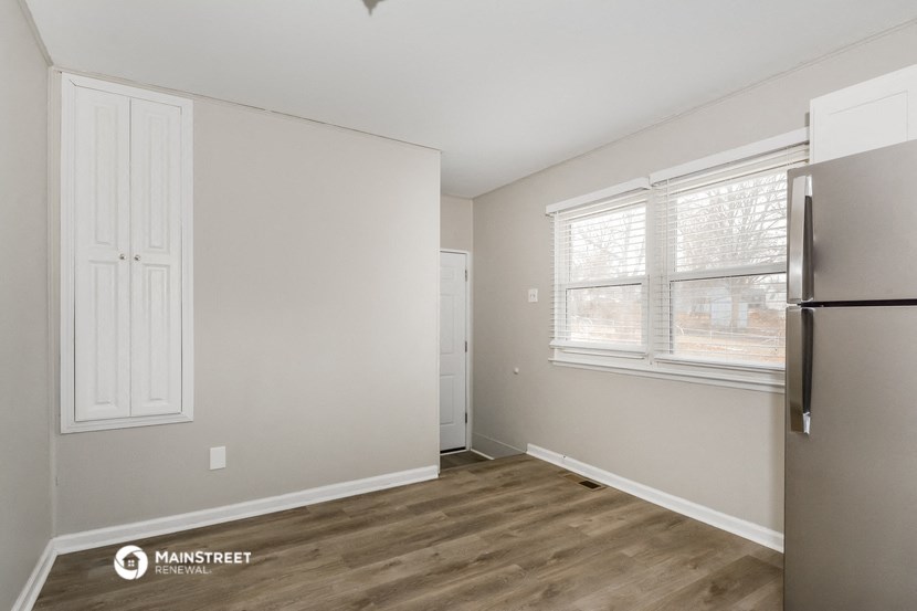 the living room of an apartment with a refrigerator and a window