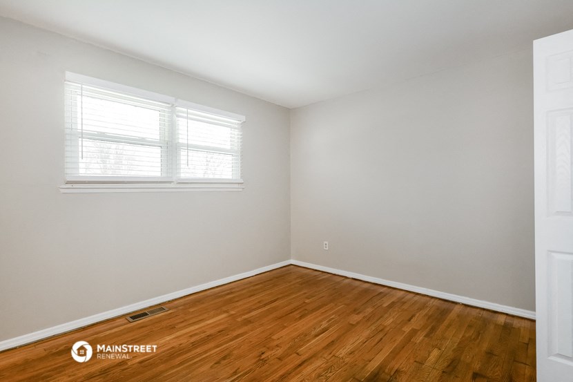 a bedroom with wood floors and white walls and a window