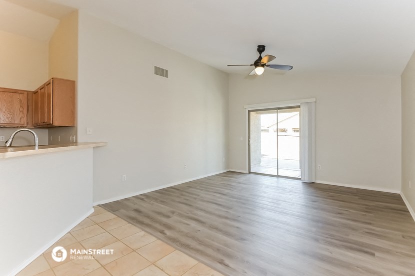 an empty living room with a kitchen and a ceiling fan