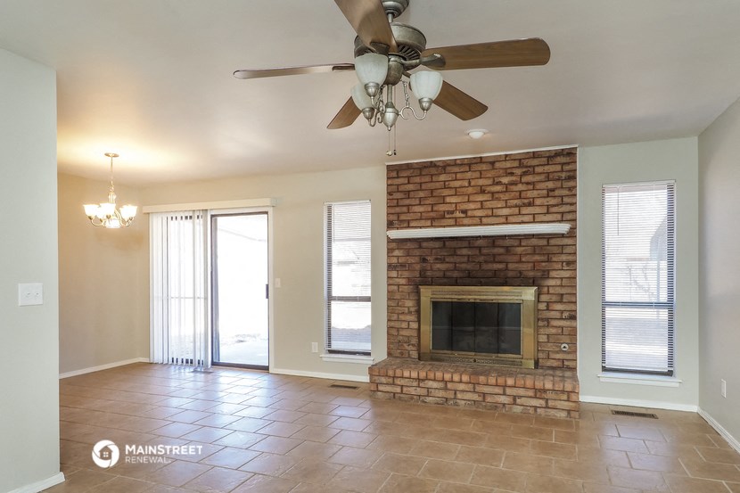 an empty living room with a brick fireplace and a ceiling fan