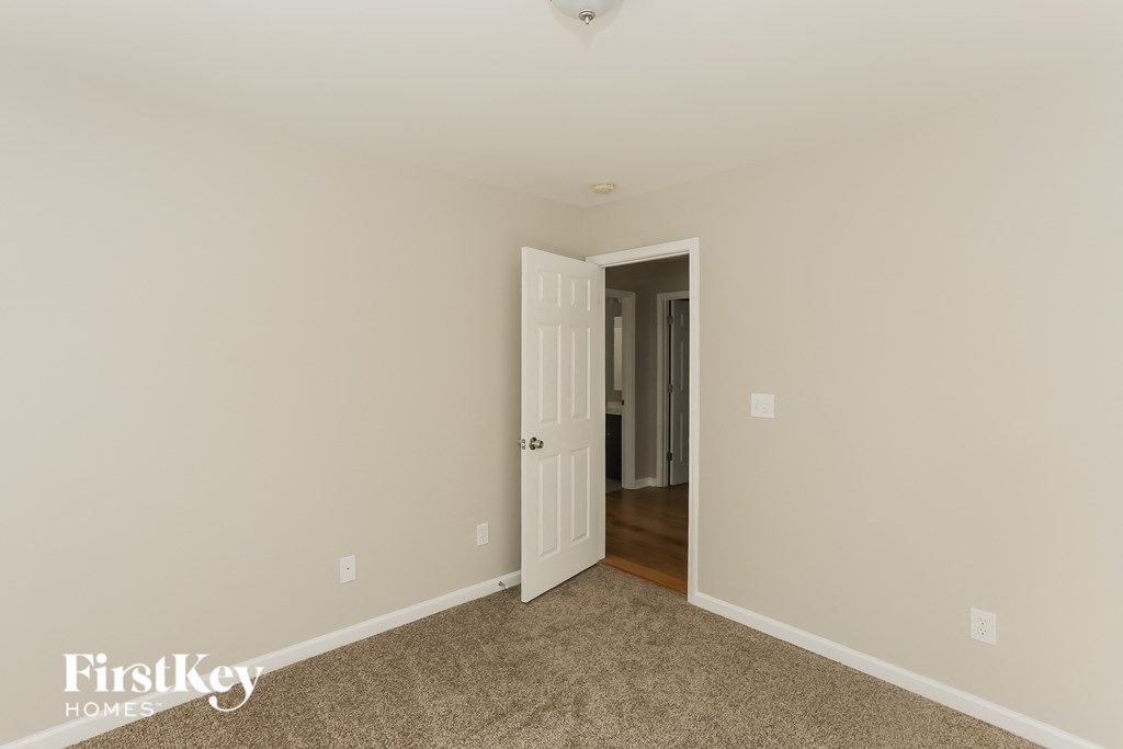 a bedroom with beige carpet and a door to a hallway