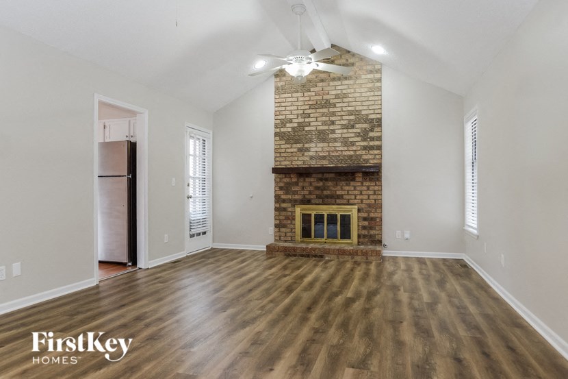 an empty living room with a brick fireplace and wooden floors