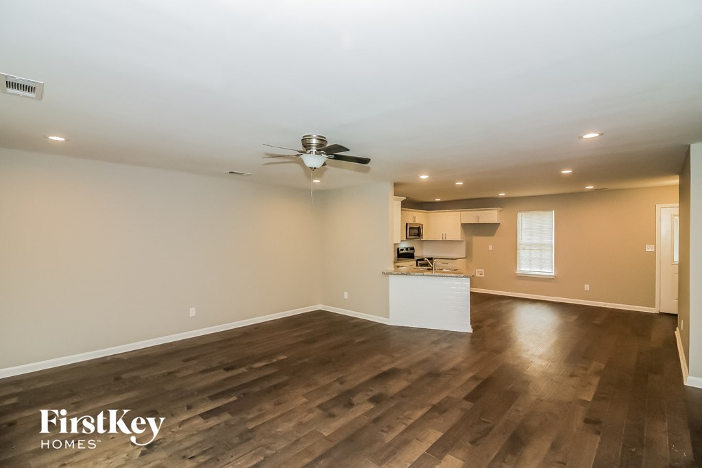 an empty living room with a ceiling fan and a kitchen