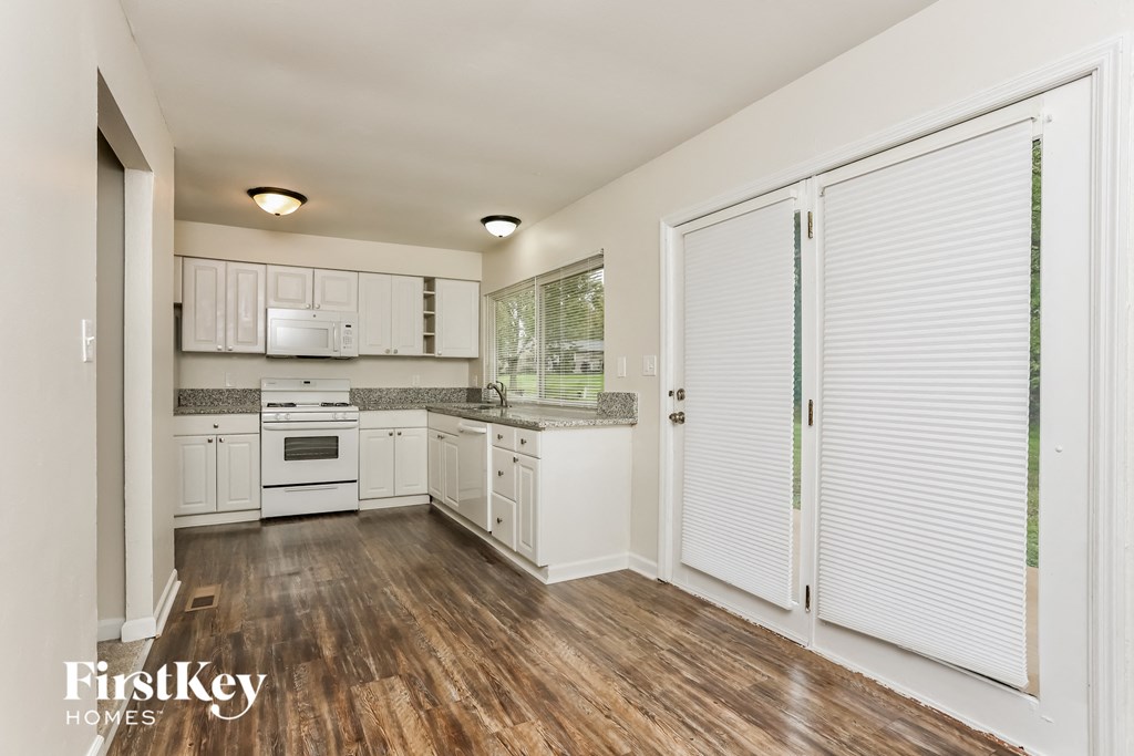 a kitchen with white cabinets and white appliances and wood flooring