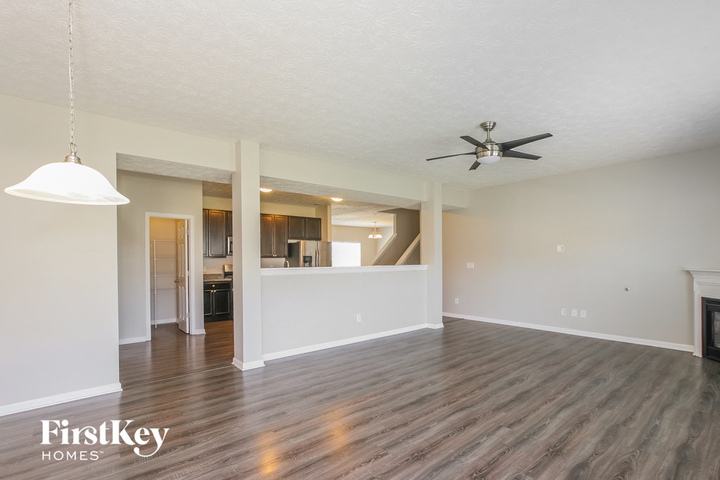 an empty living room with a ceiling fan and a kitchen