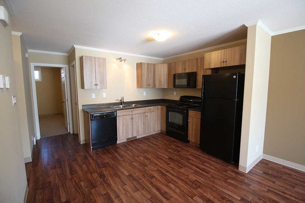 an empty kitchen with black appliances and wooden floors