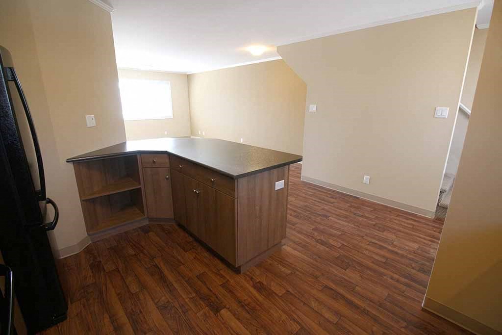 an empty room with a kitchen and wooden floors