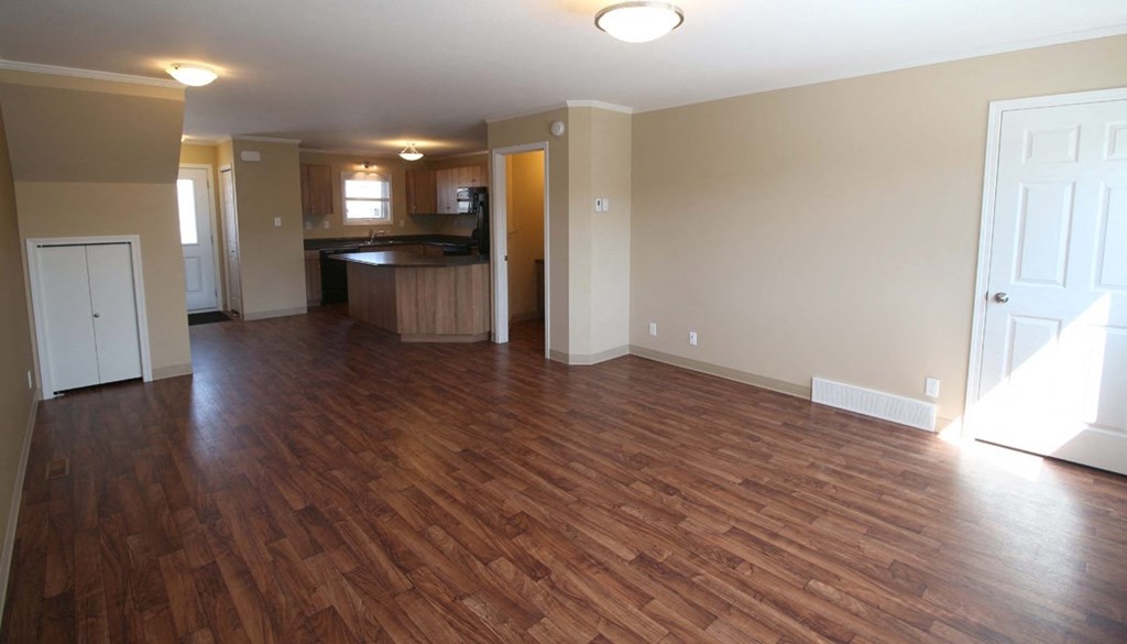 an empty living room and kitchen with wood flooring