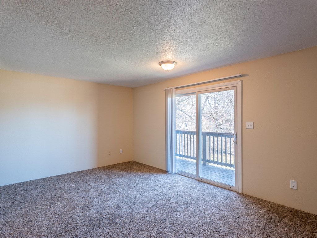 an empty living room with a sliding glass door to a balcony