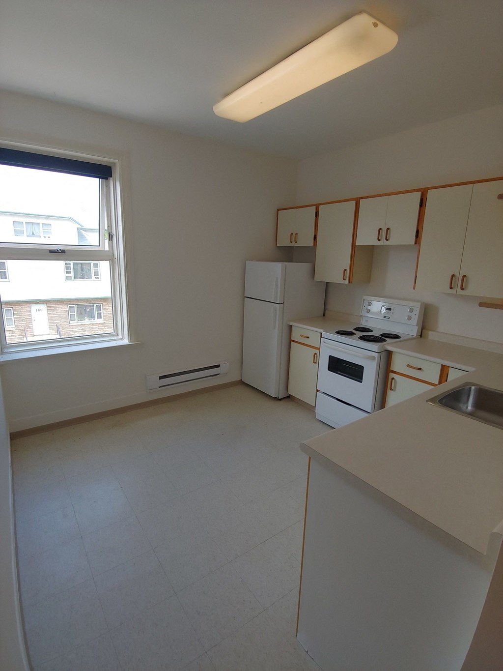 an empty kitchen with white appliances and a large window