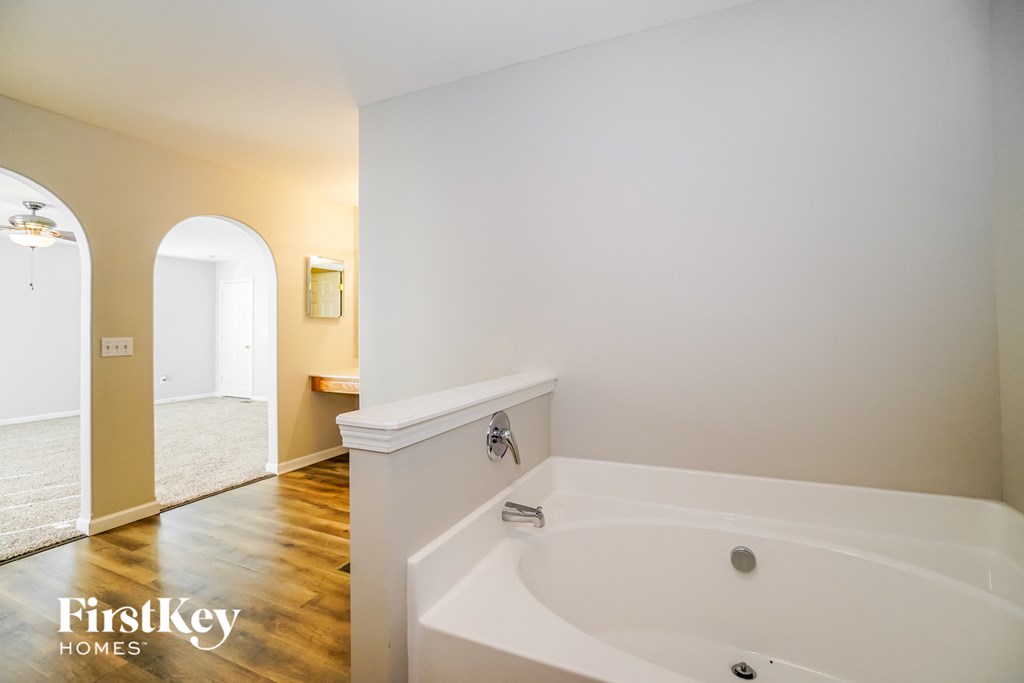 a large white bath tub in a bathroom with white walls and wood floors