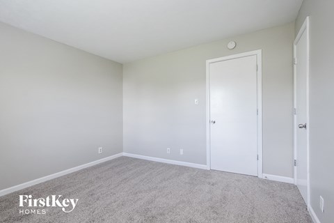 a bedroom with white walls and carpet and a door to a closet