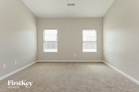 A spacious room with two windows and a carpeted floor.