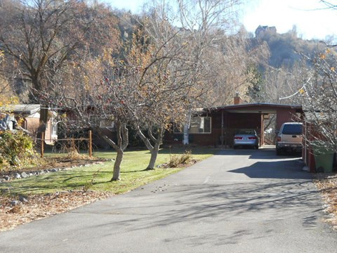 A car is parked in front of a house on a tree-lined street.