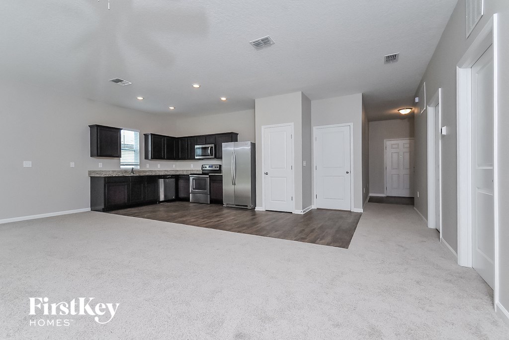 an empty living room and kitchen with a refrigerator and microwave