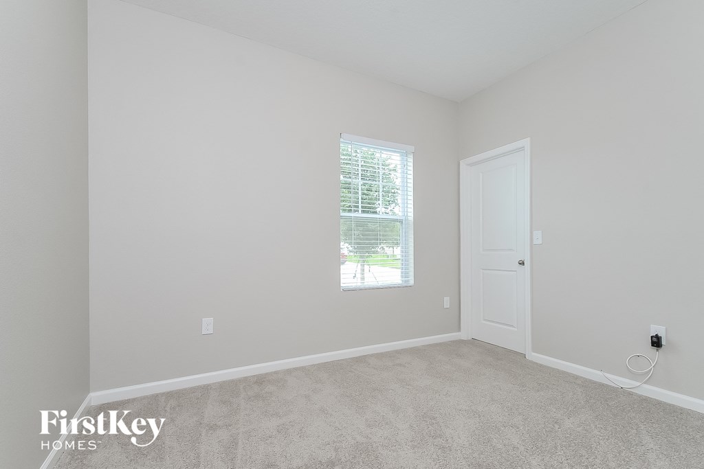 a bedroom with white walls and carpet and a window
