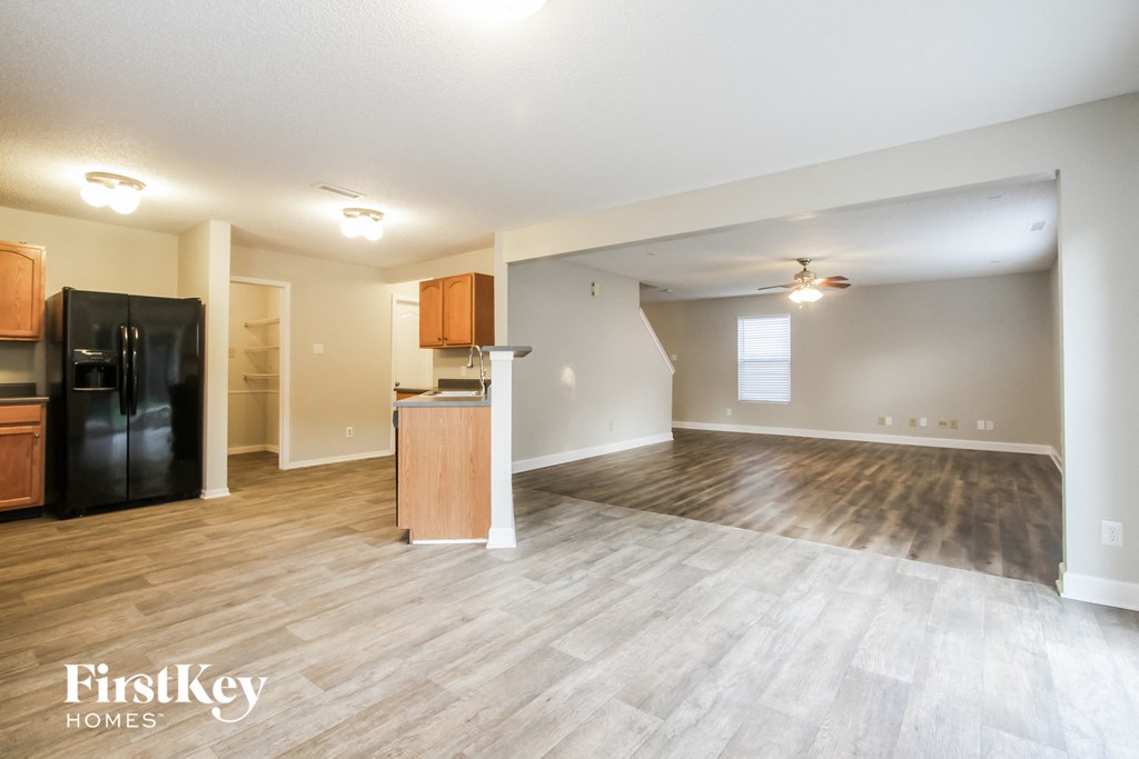 an empty living room with a kitchen and a refrigerator