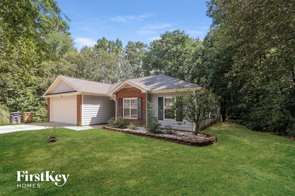 A house with a garage is surrounded by trees and has a well-manicured lawn.