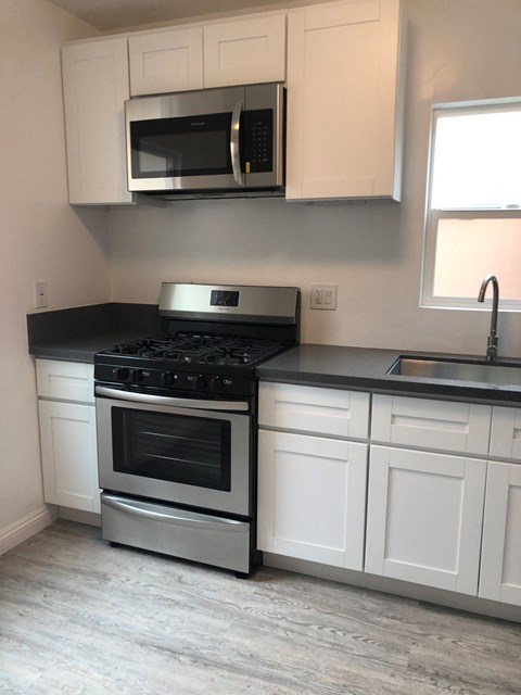 an empty kitchen with white cabinets and a stove and microwave