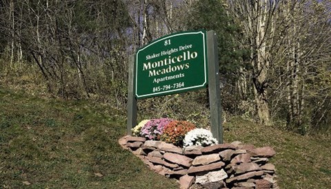 A green sign for Monticello Meadows Apartments sits on a stone wall.