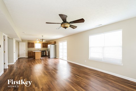 an empty living room with a ceiling fan and a kitchen
