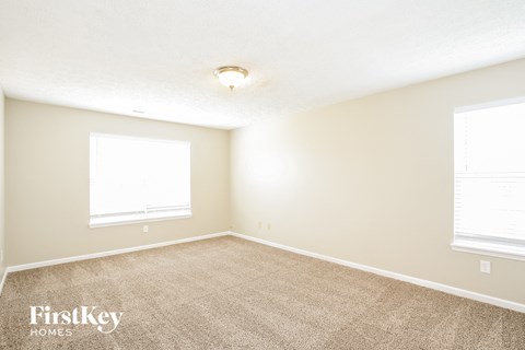 a spacious room with carpet and two windows