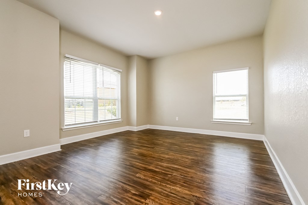 A room with wooden flooring and two windows.
