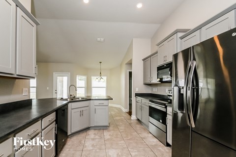 A kitchen with a stainless steel refrigerator and black countertops.