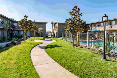 a path through the grass between two apartment buildings and a pool
