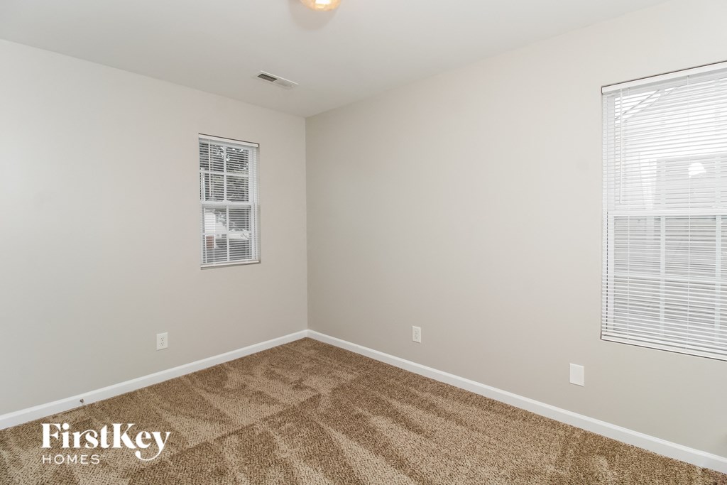a spacious room with carpeted flooring and two windows