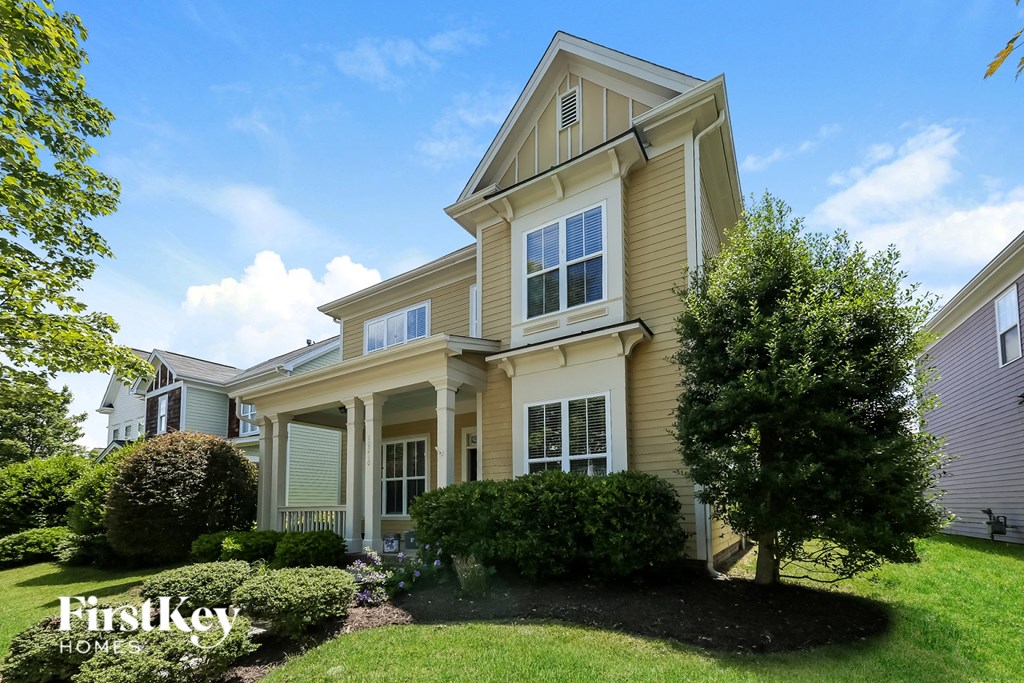 a yellow house with white trim and a tree in the yard