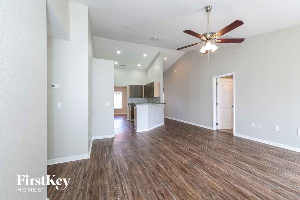 an empty living room with a ceiling fan and a kitchen