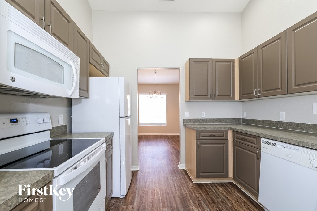 an empty kitchen with white appliances and wood flooring