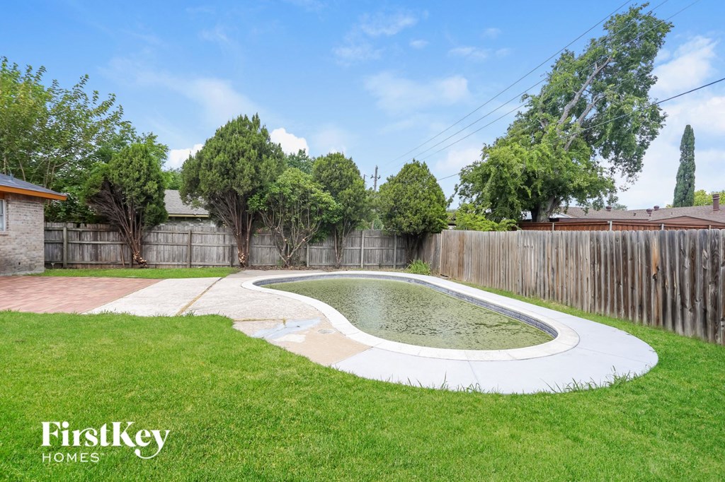 a backyard with a pool and a wooden fence and a grassy area with trees