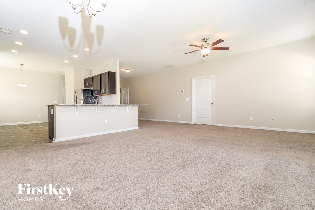 an empty living room with a kitchen and a ceiling fan