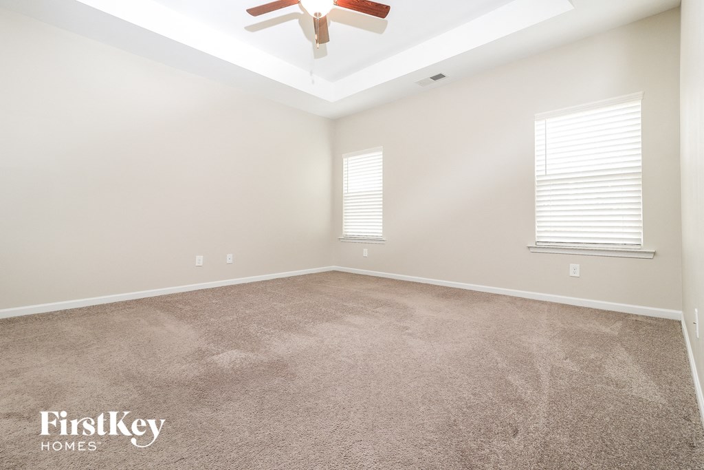 a carpeted room with a ceiling fan and two windows