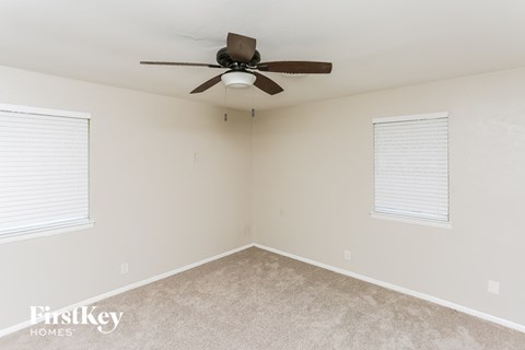 A room with a ceiling fan and two windows.