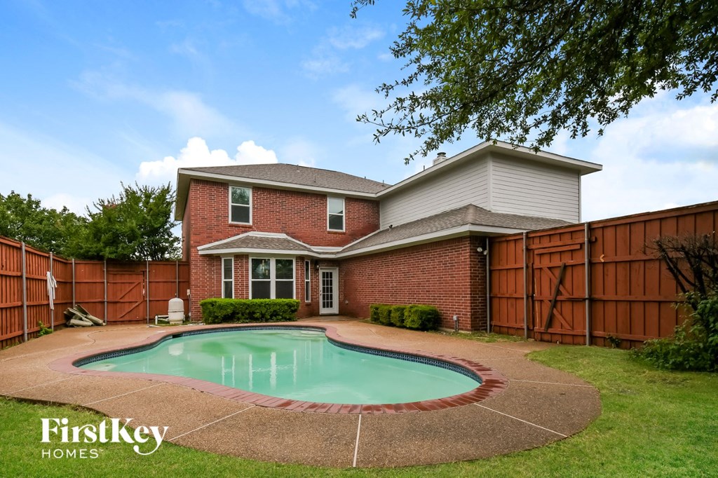 a backyard pool in front of a brick house with a wooden fence