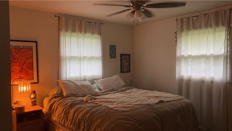 A bedroom with a bed, a ceiling fan, and a nightstand with a lamp.