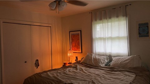 A bedroom with a bed, a ceiling fan, and a window with curtains.
