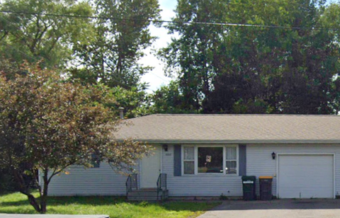 A house with a white garage door and a tree in front of it.