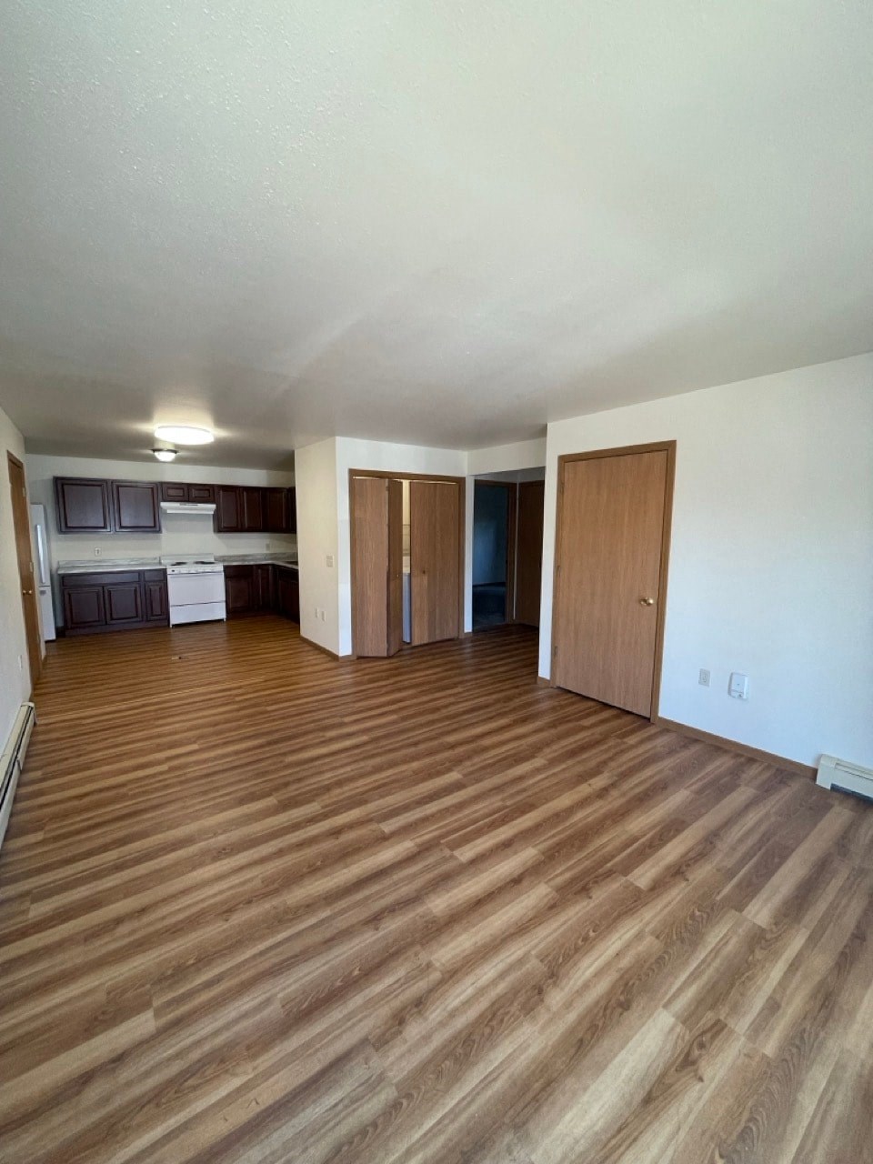 an empty living room with wood floors and a kitchen