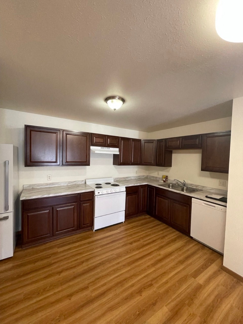 an empty kitchen with wooden floors and white appliances
